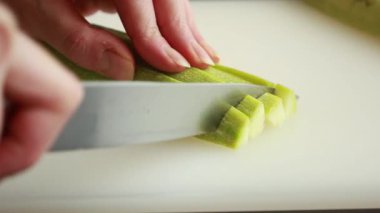 Beyaz kesme tahtasına yakın taze kabak dilimleyen bir kadın.