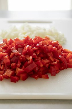 Beyaz kesim tahtasında doğranmış soğan ve kırmızı çan biberi.