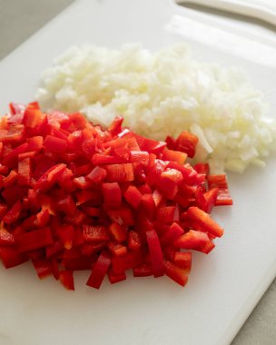 Beyaz kesim tahtasında doğranmış soğan ve kırmızı çan biberi.