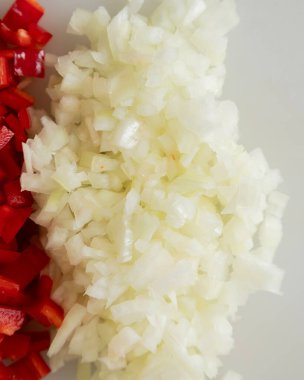 Beyaz kesim tahtasında doğranmış soğan ve kırmızı çan biberi.