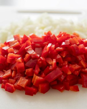 Beyaz kesim tahtasında doğranmış soğan ve kırmızı çan biberi.