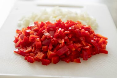 Beyaz kesim tahtasında doğranmış soğan ve kırmızı çan biberi.