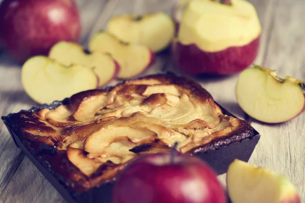 Ein Apfelkuchen und ein paar Äpfel auf einem Holztisch — Stockfoto