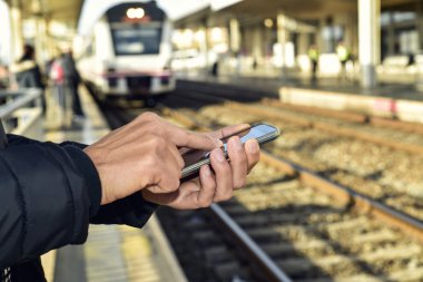 bir tren istasyonunda bir akıllı telefon kullanan genç adam