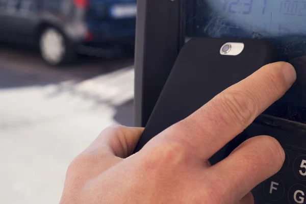 Jovem pagando com seu smartphone em um parquímetro — Fotografia de Stock