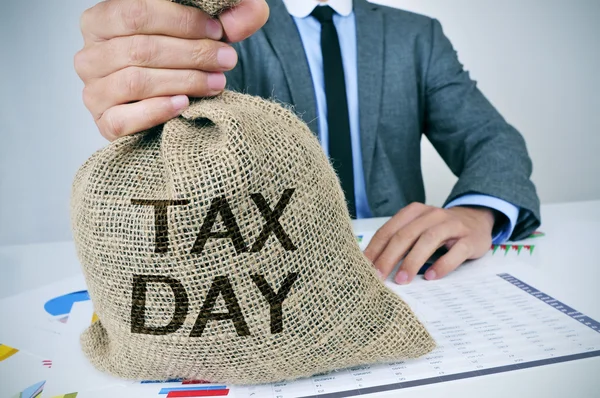 Hombre con una bolsa de dinero con el día del impuesto de texto —  Fotos de Stock