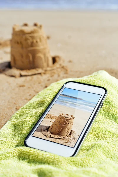 Picture of a sandcastle in a smartphone on the beach — Stock Photo, Image