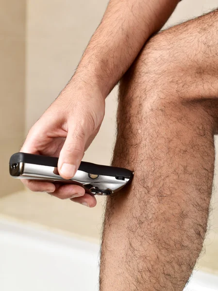 Young man trimming his legs with an electric trimmer — Stock Photo, Image