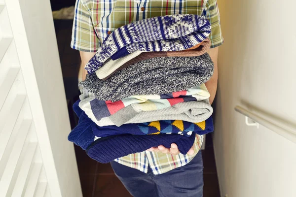 Young man with a pile of folded sweaters — Stock Photo, Image