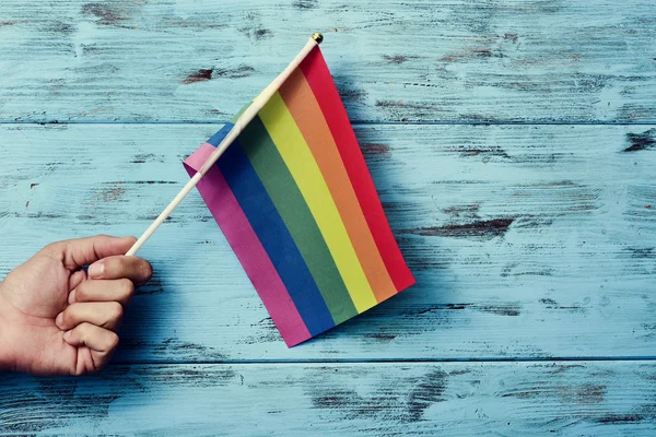 Hombre ondeando una pequeña bandera de arco iris — Foto de Stock