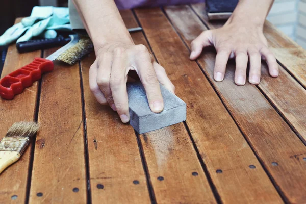 Jovem lixando uma mesa de madeira com um bloco de lixamento — Fotografia de Stock