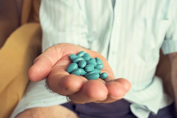 Anciano con un montón de píldoras azules en la mano — Foto de Stock