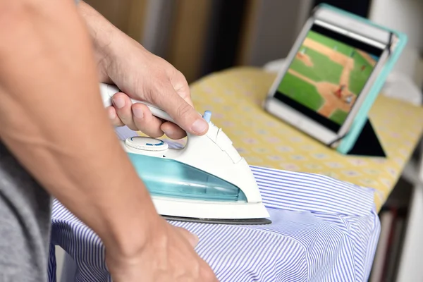 Jovem engomar uma camisa enquanto assiste esportes online — Fotografia de Stock