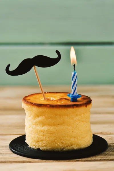 Bigode e vela acesa em um bolo de queijo — Fotografia de Stock