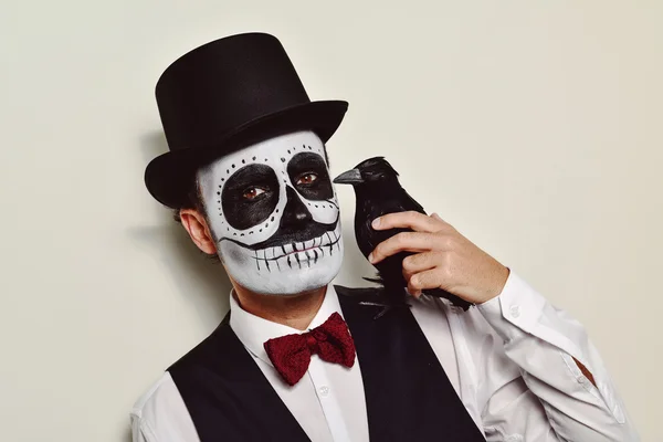 Hombre con maquillaje de calaveras y un cuervo negro — Foto de Stock