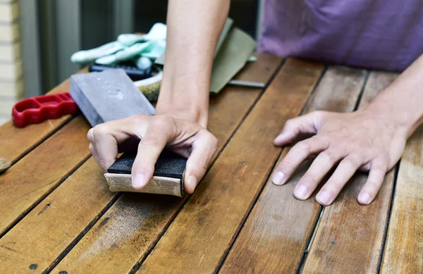 Young man sanding a wooden table with a sanding block — Stock Photo, Image