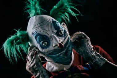 Rahatsız edici, yeşil saçlı, kirli kırmızı bir kostüm, kirli bir papyon takan, kirli ve kanlı eldivenler takan iğrenç bir yüz maskesi takan ya da çıkartan kötü kalpli bir palyaçoya yakın plan.