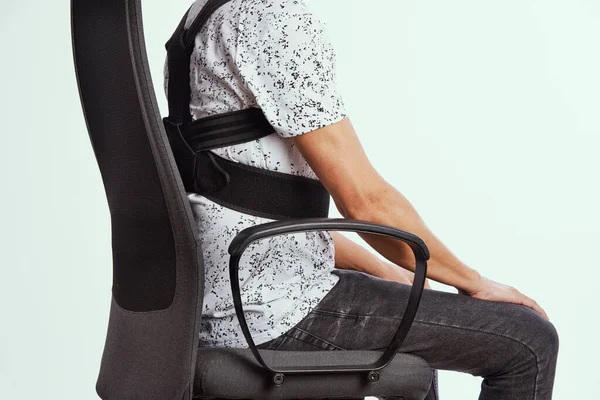 オフィスの椅子に座っている若い白人男性の背中の姿勢補正器を身に着けている — ストック写真