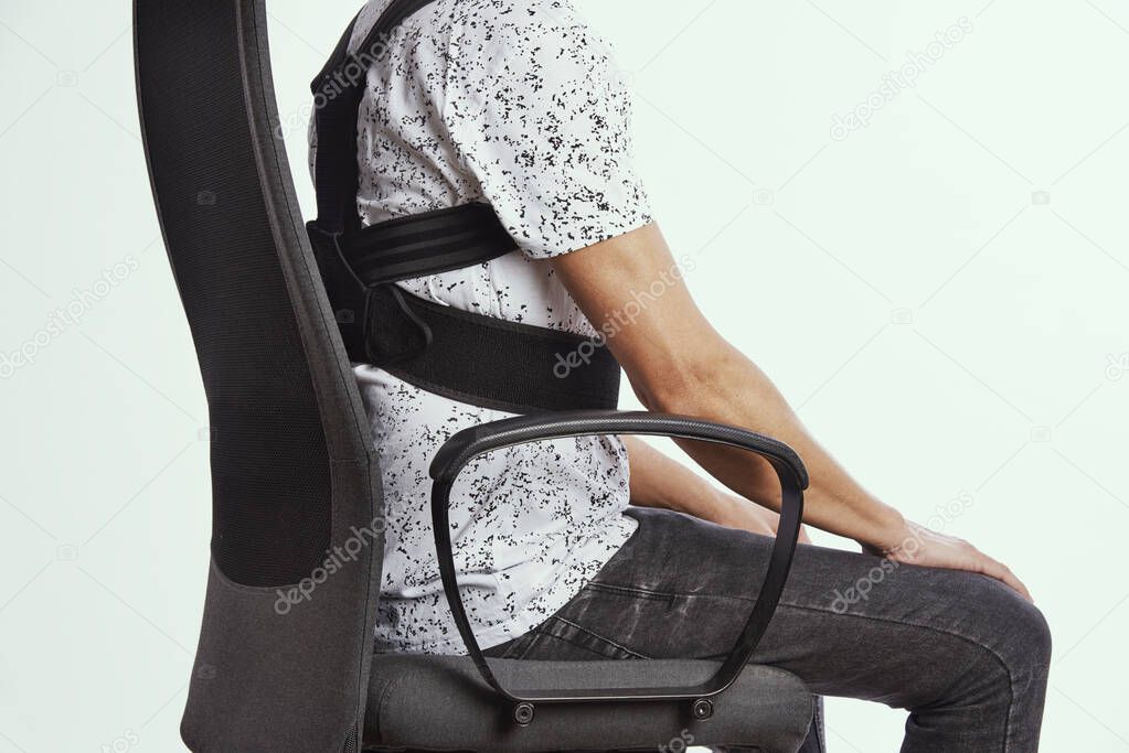 closeup of a young caucasian man wearing an upper back posture corrector as is sitting at his office chair