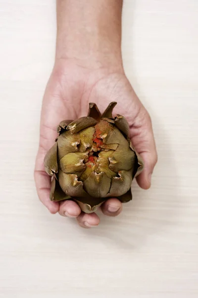 在一张白色的木制桌子上 一个男人抓起用木瓜调味的熟朝鲜蓟的手的高角图像 — 图库照片