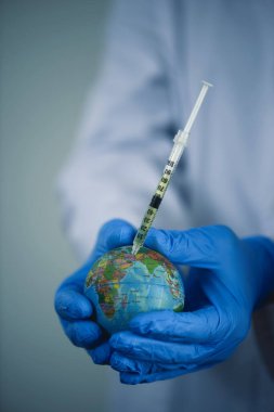 Beyaz önlüklü, mavi eldivenli, karasal bir küreyi aşılayan bir doktor.
