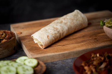 Bir masanın üzerinde soğan, kırmızı ve yeşil biber, taze marul ve salatalık gibi farklı sebzelerle pişirilmiş tavuk etiyle dolu bir balık ya da burrito yakın plan.