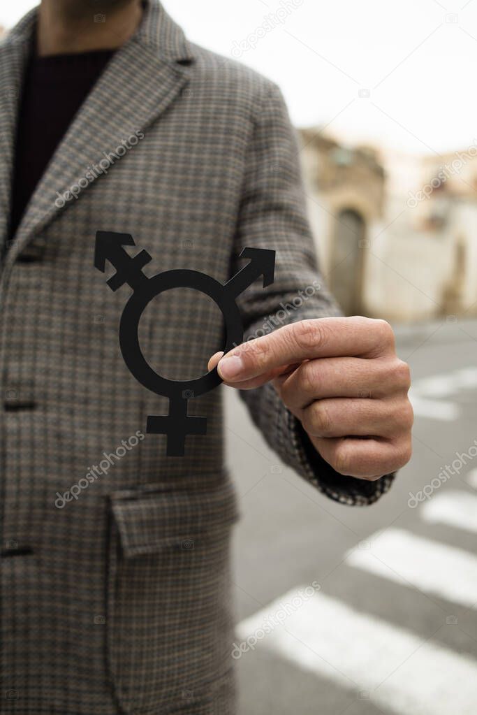 closeup of a young caucasian person standing on the street, wearing a coat, showing a transgender symbol