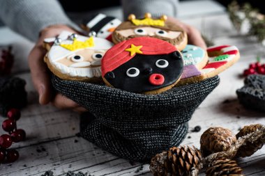 closeup of a young caucasian man with knitted bag in his hand with a pile of christmas cookies with different shapes and colors, such as the three wise men, a snowman or a candy cane clipart
