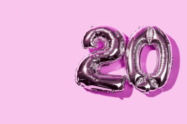 20 sayısını oluşturan iki numara şekilli balon, solunda boş bir alan olan pembe bir zemin üzerinde.