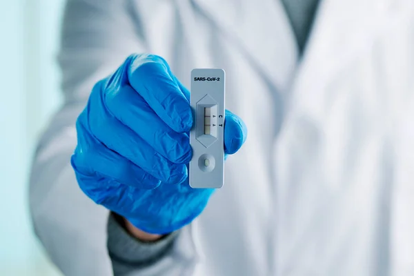 医疗工作者的特写镜头 身穿白色外套 戴着蓝色手术手套 手里拿着一个Covid 19测试装置 显示出阳性结果 — 图库照片