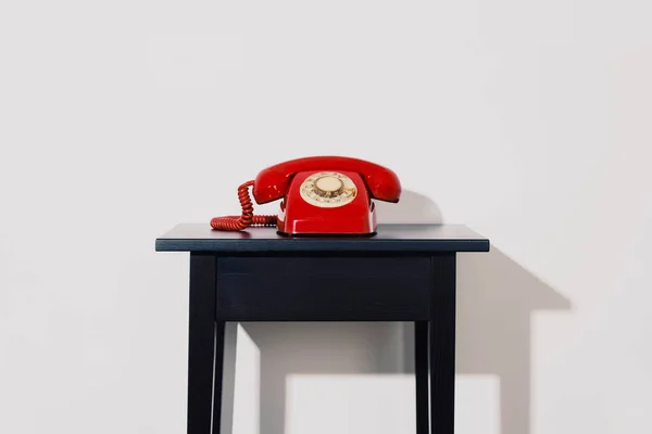 白い壁の前の黒い木製のテーブルの上に赤い固定電話の回転式ダイヤル電話 — ストック写真