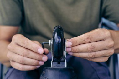 Yeşil tişörtlü ve gri pantolonlu genç bir beyaz adamın yakın çekimi. İç patenin tekerleklerini değiştirmek için uğursuz anahtar kullanıyor.