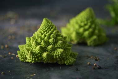 Bazı çiğ bebek romanesco brokoli başları farklı otlar, baharatlar ve tohumlar serpiştirilmiş karanlık bir taş yüzeyine serpilmiş.