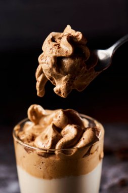 Birisi bardaktan bir kaşık dalgona kahvesi alıyor, gri arka planda koyu gri bir taş yüzeye yerleştiriliyor.