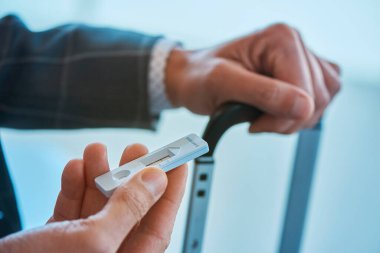 Zarif gri takım elbiseli, genç bir işadamının elinde, elinde, bir havaalanının bekleme salonunda otururken, negatif sonuç veren, çovid-19 antijen test cihazı var.