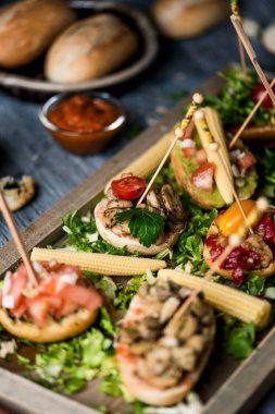 Tahta bir tepsi yakın çekim, bazı farklı vejetaryen pinchos farklı malzemelerle yapılmış, aperatif veya aperatif olarak sunulan gri rustik ahşap masa üzerinde