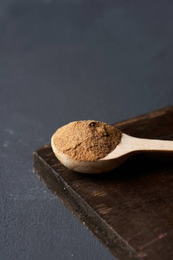 Kamuflaj tozu dolu ahşap bir kaşığa yakın plan. Koyu gri bir yüzeye yerleştirilmiş, üzerinde boş bir alan var.