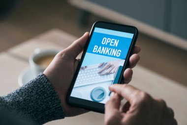 Kafkasyalı genç bir adamın elinde akıllı telefonu var, ekranında açık bankacılık metnini okuyor.