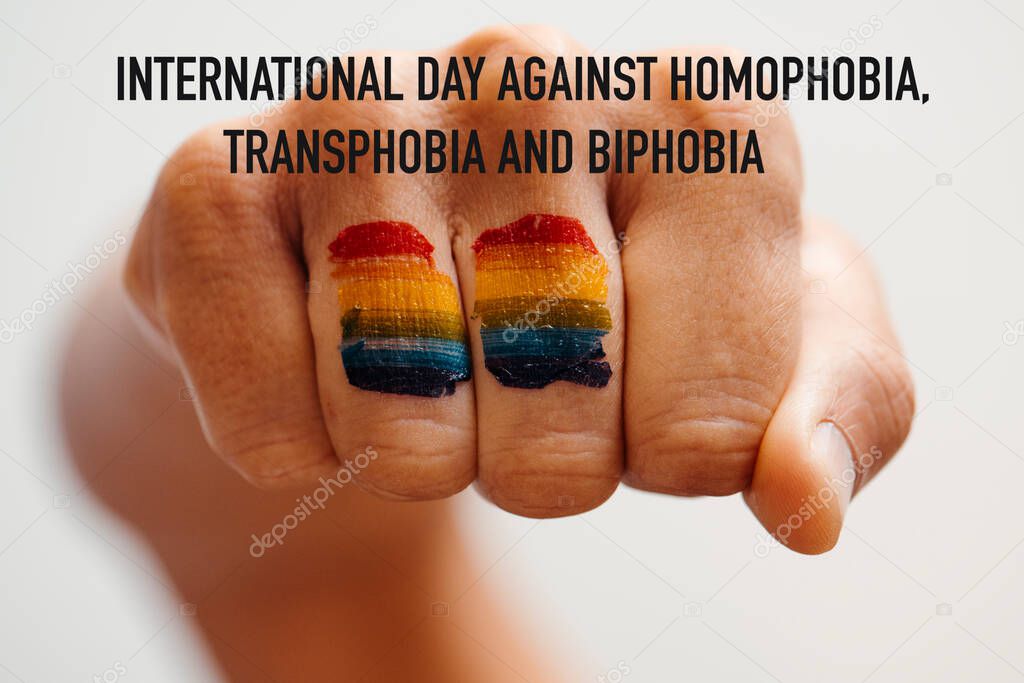 the rainbow flag painted in the fist of a young person and the text international day against homophobia, transphobia and biphobia