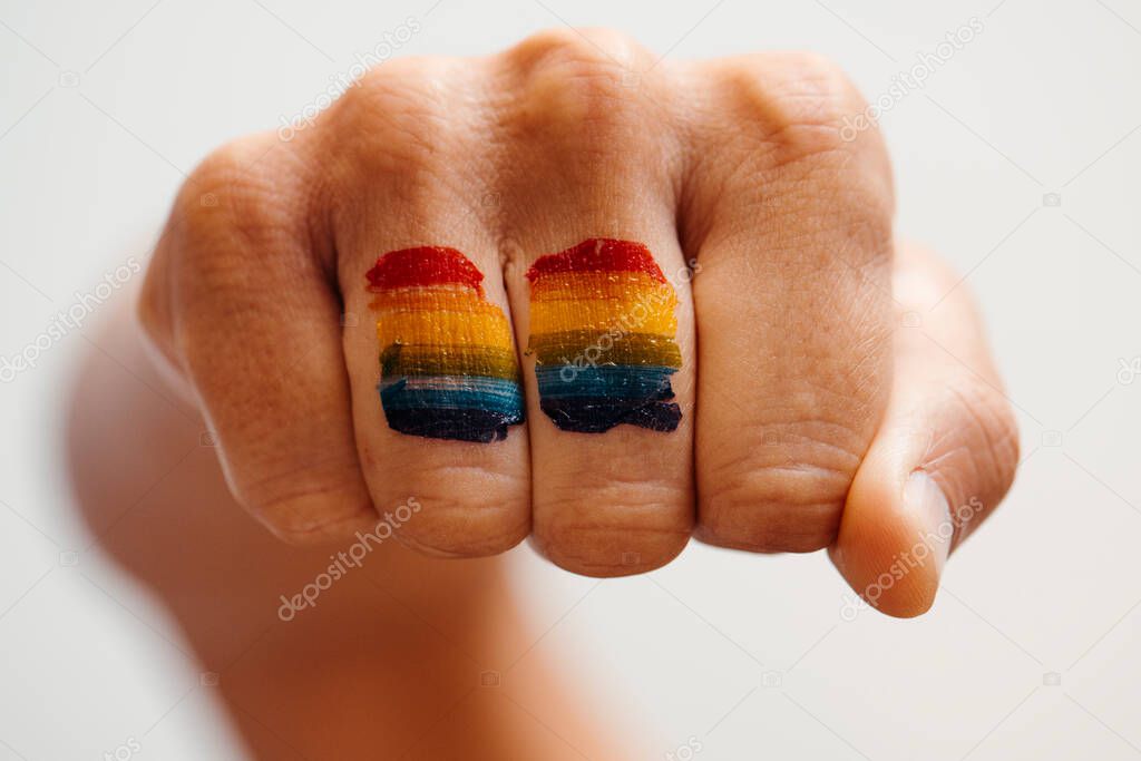 closeup of the rainbow flag painted in the fist of a young caucasian person, against an off-white background