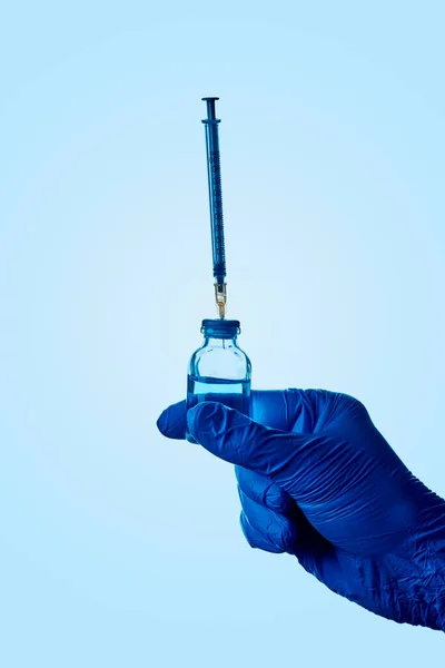 青い手術用手袋を着用し青い液体のバイアルとそのストッパーに刺さった注射器を持っている医療従事者又は研究室の労働者の閉鎖 — ストック写真