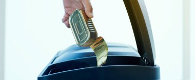 Genç bir adamın boş bir teneke kutuyu web pankartı veya başlık olarak kullanmak üzere panoramik bir formatta eve geri dönüşüm kutusuna atması