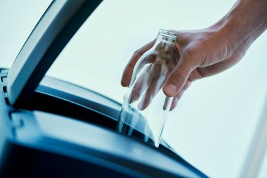 Kafkasyalı genç bir adamın, bir ev geri dönüşüm kutusunun cam bölmesine boş bir cam şişe attığı yakın plan.