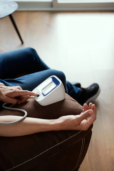 stock image closeup of a caucasian man measuring his blood pressure with an electronic sphygmomanometer, sitting on a brown sofa