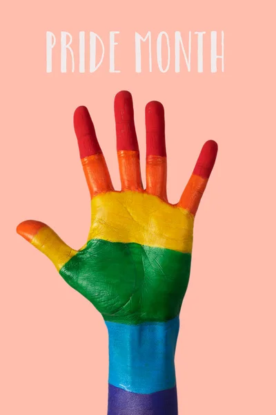 the hand of a man, painted as the rainbow flag, and the text pride month against a pale pink background