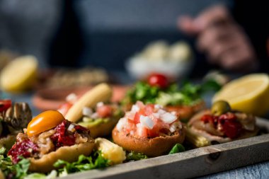 some different vegan appetizers, with different toppings, on a wooden tray, on a gray rustic wooden table, and a man sitting at the table in the background