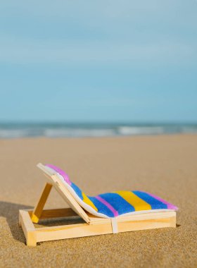 a miniature deck chair on the sand of a lonely beach, with the sea in the background and some blank space on top