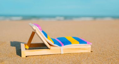 Plajda minyatür bir iskemle, arka planda deniz, web pankartı veya başlık olarak kullanılacak panoramik bir formatta.