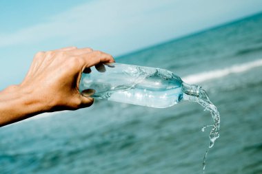 Kafkasyalı genç bir adam okyanusun önündeki tekrar kullanılabilir su şişesinden su dolduruyor.