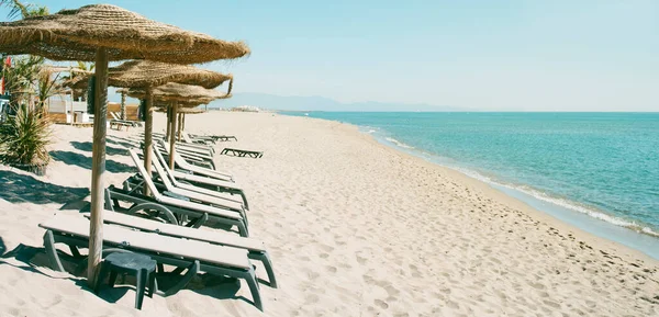 一些用天然材料制成的遮阳伞和一些米色的日光浴者 在安静的海滩上 以全景形式使用 作为网页横幅或标题 — 图库照片